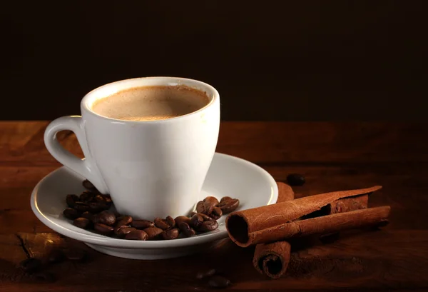 Tasse mit Kaffee, Zimt und Kaffeebohnen auf Holztisch auf braunem Backblech — Stockfoto