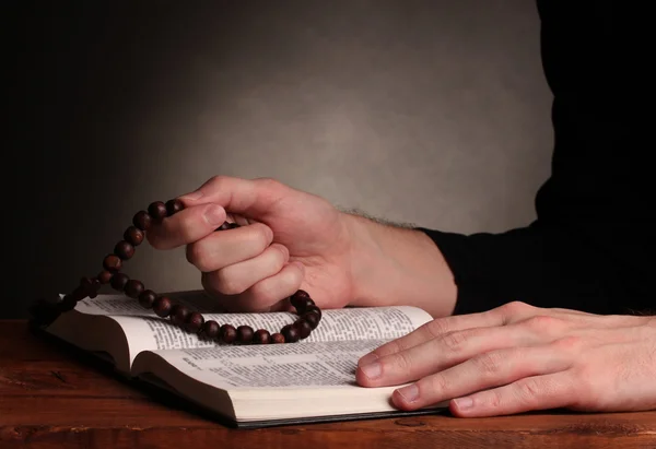 Mani che tengono il rosario di legno sopra la santa bibbia russa aperta su sfondo grigio — Foto Stock