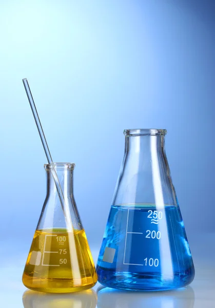 Zwei Kolben mit gelber und blauer Flüssigkeit mit Reflexion auf blauem Hintergrund — Stockfoto