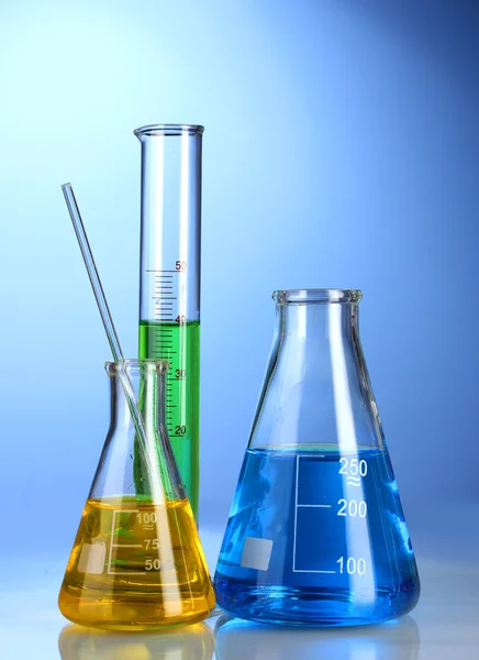 Três frascos com líquido colorido com reflexão sobre fundo azul — Fotografia de Stock