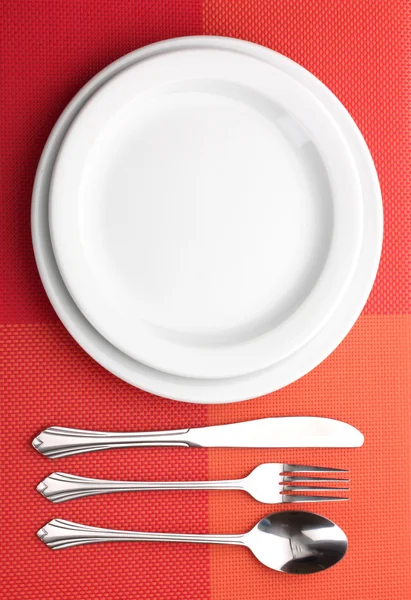 Біла порожня тарілка з виделкою, ложкою та ножем на червоній скатертині — стокове фото
