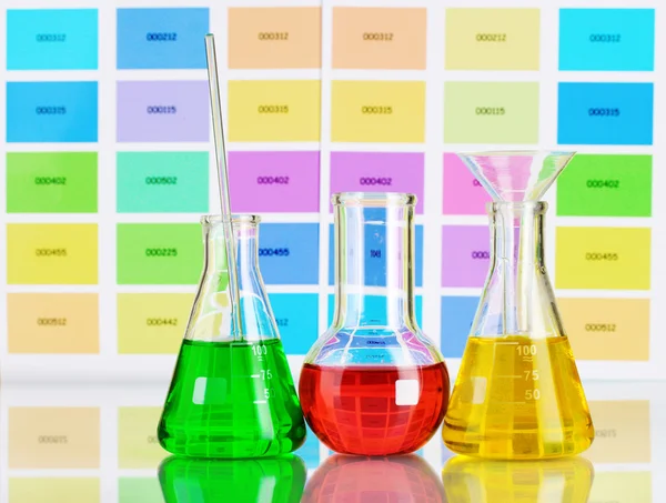 Three flasks with color liquid on color samples background — Stock Photo, Image