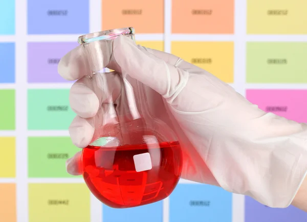 Flask with red liquid in hand on color samples background — Stock Photo, Image