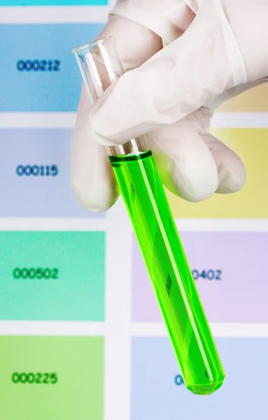 Tube with green liquid in hand on color samples background — Stock Photo, Image