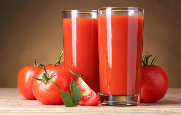 Tomato juice in glasses and tomato on wooden table on brown back