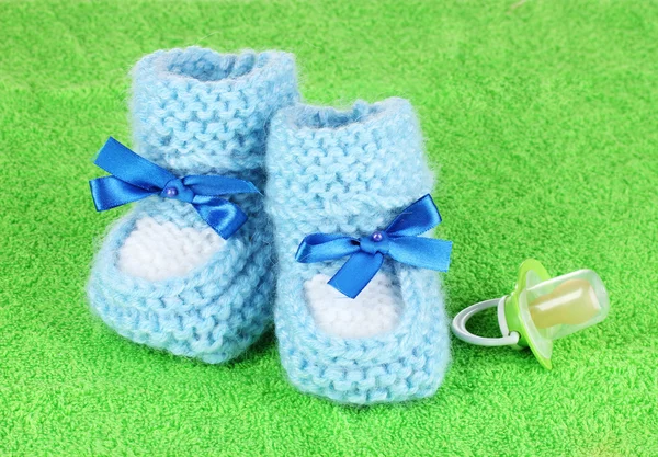Botines de bebé azul y chupete sobre fondo verde — Foto de Stock