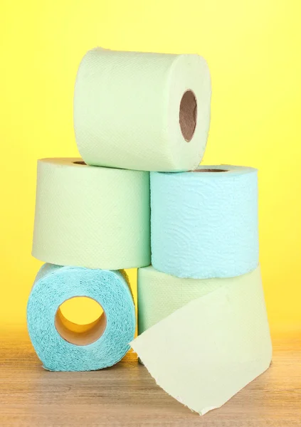 Green and blue rolls of toilet paper on wooden table on yellow background Royalty Free Stock Photos