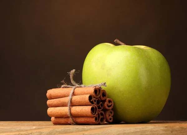 Varas de canela e maçã verde na mesa de madeira no fundo marrom — Fotografia de Stock