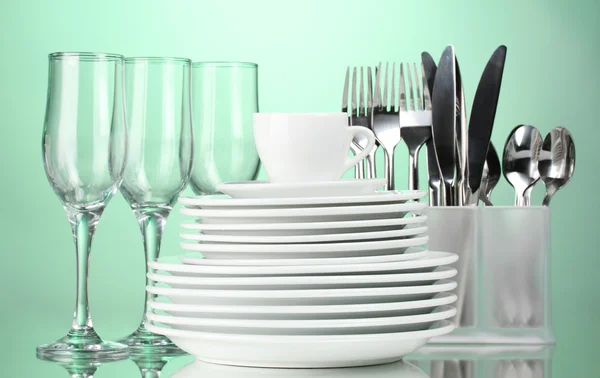 Clean plates, glasses, cup and cutlery on green background — Stok fotoğraf