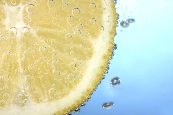 Zitronenscheibe im blauen Wasser mit Blasen — Stockfoto