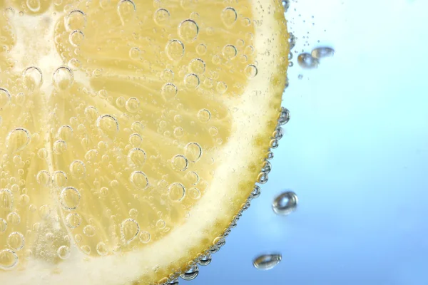 stock image Slice of lemon in the blue water with bubbles