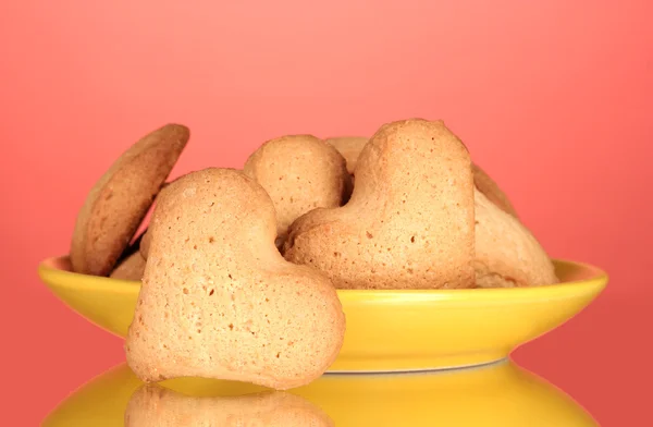 Kırmızı arka planda sarı tabakta kalp şeklinde kurabiyeler. — Stok fotoğraf