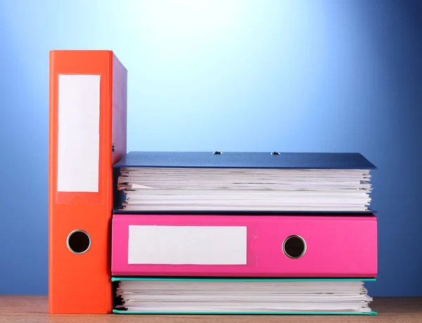 Jasne biuro foldery na drewnianym stole na niebieskim tle — Zdjęcie stockowe
