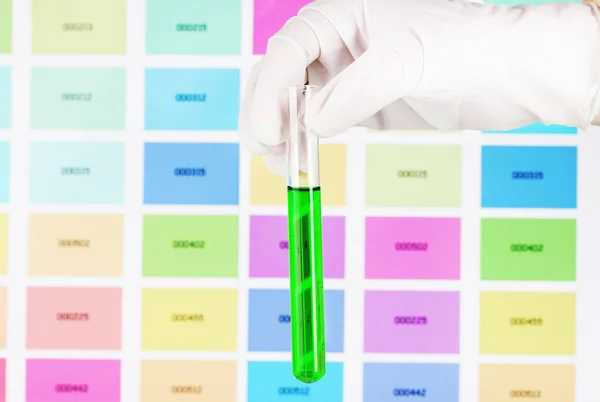 Tubo con líquido verde en la mano sobre el fondo de muestras de color — Foto de Stock
