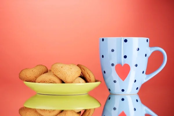 Herzförmige Kekse auf Teller und Tasse mit Teebeutel auf rotem Hintergrund — Stockfoto