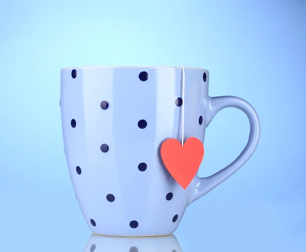 Taza azul y bolsa de té con etiqueta roja en forma de corazón sobre fondo azul — Foto de Stock