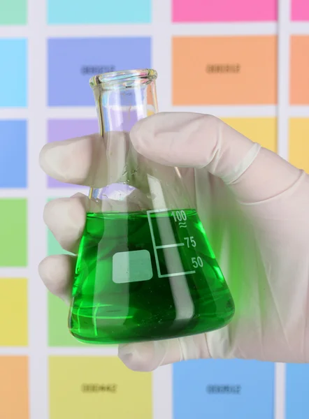 Kolven med grön vätska i handen på färg prover bakgrund — Stockfoto