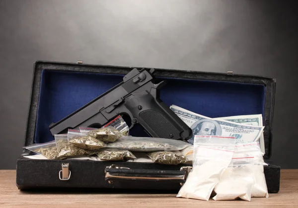 Κοκαΐνης, μαριχουάνα δολάρια και πιστόλι σε περίπτωση στο ξύλινο τραπέζι σε γκρι πίσω — Φωτογραφία Αρχείου