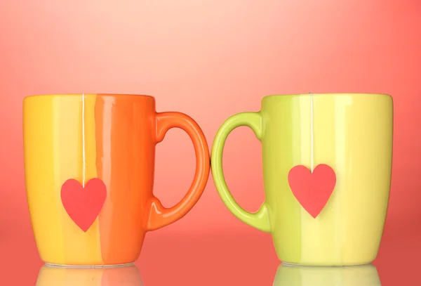 Twee kopjes en thee zakjes met rood hart-vormige label op rode achtergrond — Stockfoto