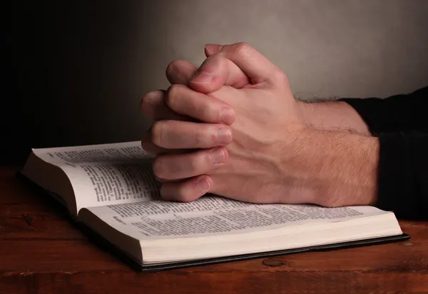 Ręce złożone w modlitwie na Pismo Święte na drewnianym stole na szarym tle — Zdjęcie stockowe