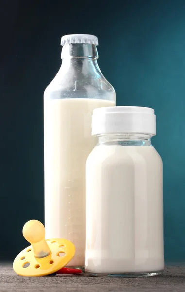 Bottiglie di latte e succhietto su tavolo di legno su fondo blu — Foto Stock