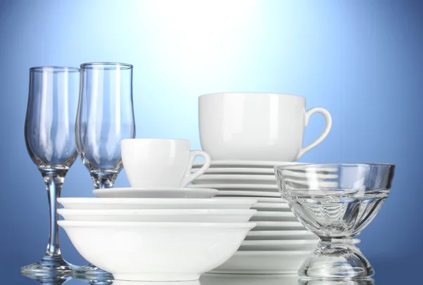 Bols vides, assiettes, tasses et verres sur fond bleu — Photo