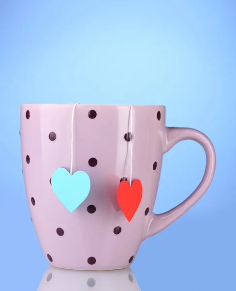 Pink cup and two tea bags with red and blue heart-shaped label on blue back — Stock Photo, Image