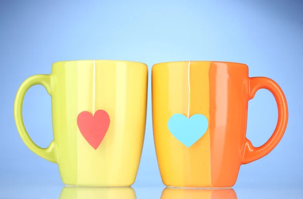 Dwie szklanki i torebki herbaty z czerwony i niebieski-serce etykiety na niebieski backgrou — Zdjęcie stockowe