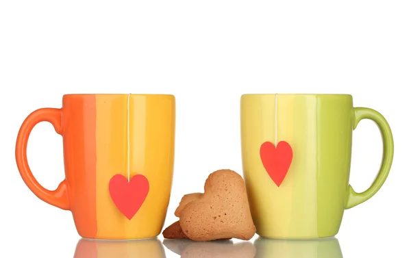 Duas xícaras com saco de chá e biscoitos em forma de coração isolados em branco — Fotografia de Stock