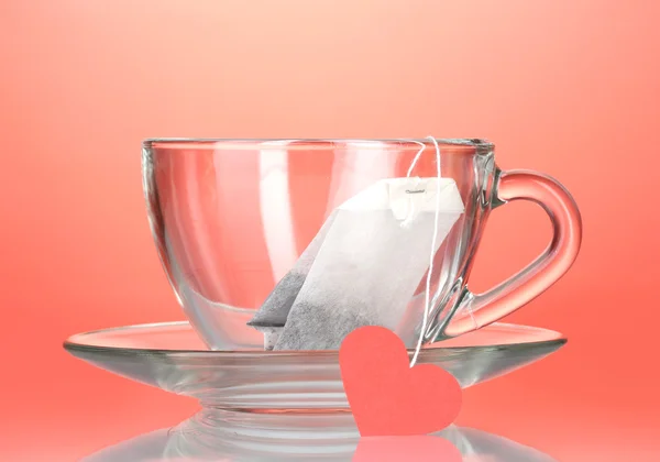 Tazza di vetro con piattino e bustina di tè con etichetta rossa a forma di cuore sul retro rosso — Foto Stock