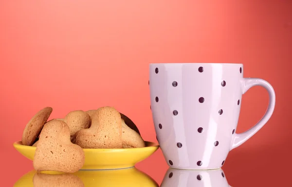 Печенье в форме сердца на желтой тарелке и чашка на красном фоне — стоковое фото