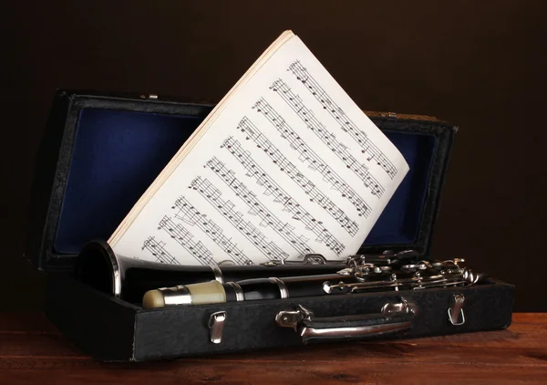 Old clarinet and notebook with notes in case on wooden table on brown backg — Stock Photo, Image