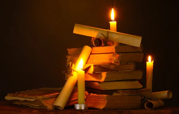 Stapel alter Bücher mit Kerze und Schriftrolle im Dunkeln — Stockfoto