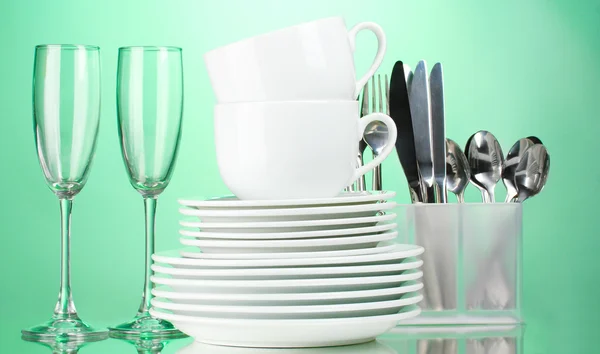 Clean plates, glasses, cups and cutlery on green background — Stock Photo, Image