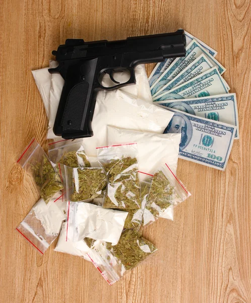 Kokain och marijuana i paket, dollar och pistol på trä bakgrund — Stockfoto