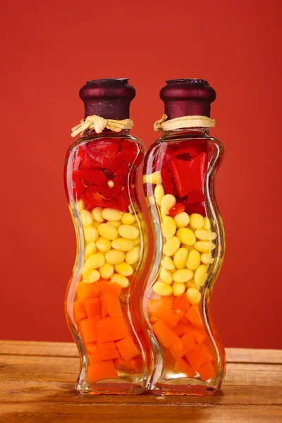 Two bottles with red pepper, beans, carrots for kitchen decor on red backgr — Stock Photo, Image