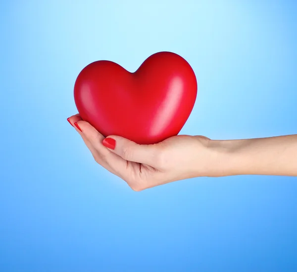 Κόκκινη καρδιά στο γυναικείο χέρι σε μπλε φόντο — Φωτογραφία Αρχείου