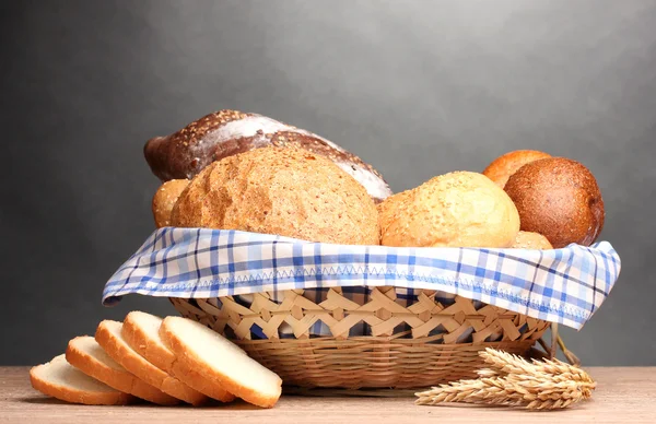 Delizioso pane in cesto e orecchie su tavolo di legno su sfondo grigio — Foto Stock