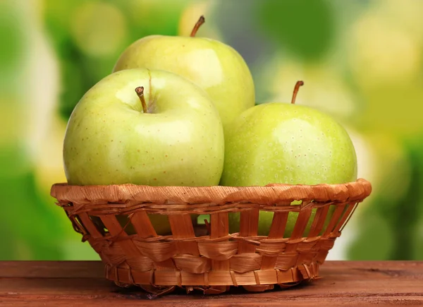 Saftige grüne Äpfel im Korb auf Holztisch auf grünem Hintergrund — Stockfoto