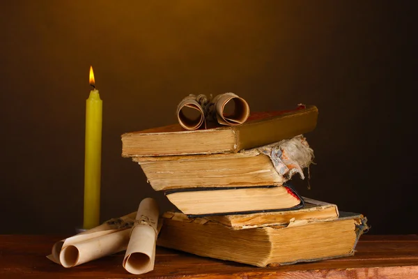 Pile of old books with candle and scroll on brown — Stock Photo, Image