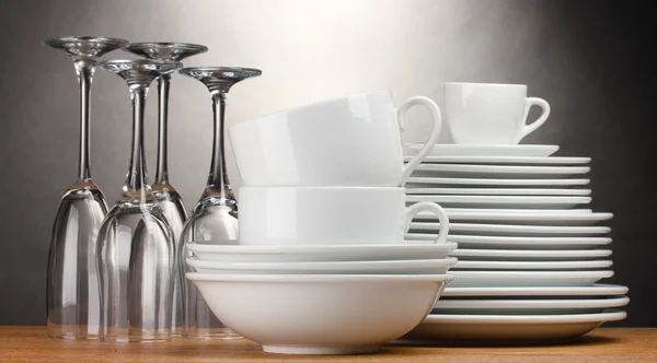 Čisté talíře, sklenice a kelímky na dřevěný stůl na šedém pozadí — Stock fotografie
