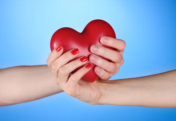 Homem e mulher segurando coração vermelho nas mãos sobre fundo azul — Fotografia de Stock