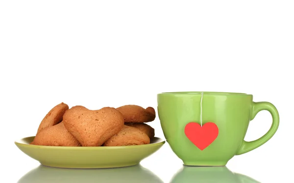 Green cup with tea bag and heart-shaped cookies on green plate isolated on — Stock Photo, Image