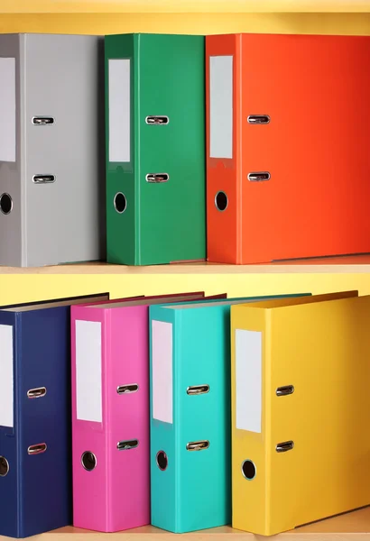 Bright office folders on wooden shelfs on yellow background Royalty Free Stock Photos