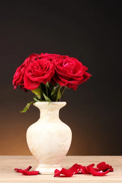 Krásné červené růže ve váze na dřevěný stůl na hnědé pozadí — Stock fotografie