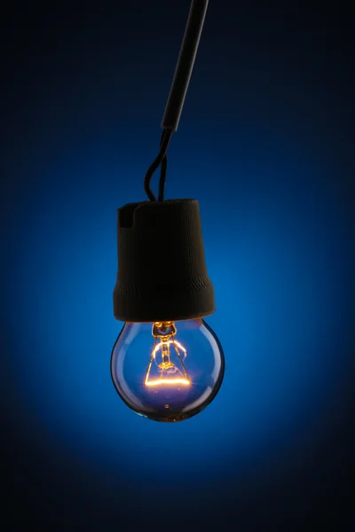 En tänd glödlampa på blå bakgrund — Stockfoto