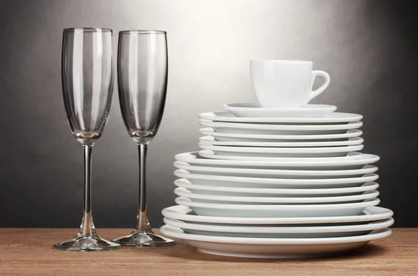 Assiettes propres, verres et tasse sur table en bois sur fond gris — Photo