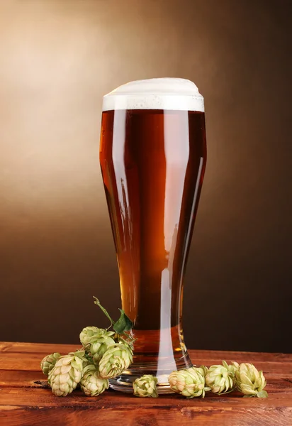 Beer in glass and green hop on wooden table on brown background — Stock Photo, Image