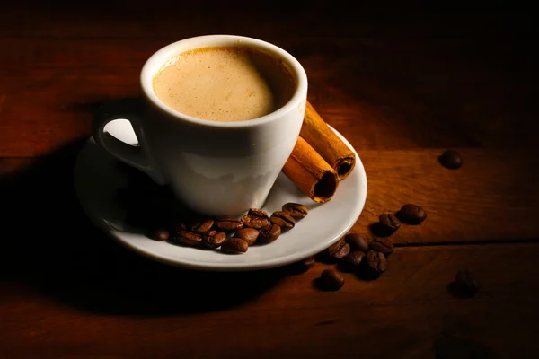 Hrnek s kávou, skořice a káva fazole na dřevěný stůl — Stock fotografie