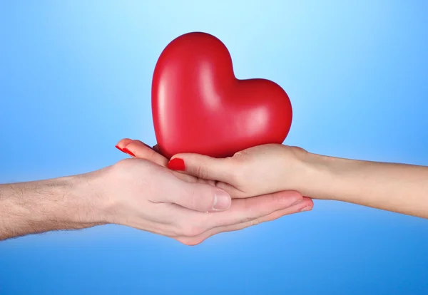 Homem e mulher segurando coração vermelho nas mãos sobre fundo azul — Fotografia de Stock